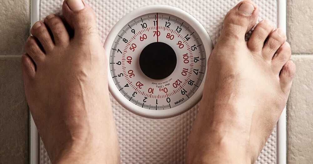 a mans feet on some scales as he is seeing if the keto diet is any good and made him lose weight